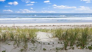 Une plage avec des dunes de sable et de l’herbe au premier plan, qui s’étend jusqu’à l’océan.
