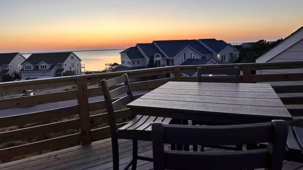 A wooden deck with a table and chairs overlooking a row of houses at sunset. - NanDUCKet on the bay in DUCK, NC! (Kitty Hawk)