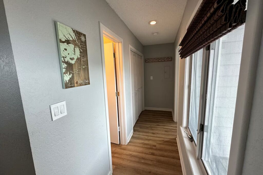 A hallway with wooden flooring, a light switch, and a door leading to another room.