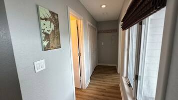 A hallway with wooden flooring, a light switch, and a door leading to another room.