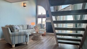 A living room with a striped sofa, a round coffee table, and a staircase. - NanDUCKet on the bay in DUCK, NC! (Kitty Hawk)
