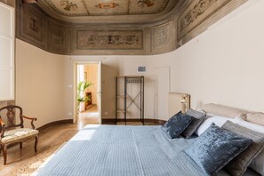 Ein Schlafzimmer mit einem großen Bett, einem hölzernen Stuhl, einem Heizkörper und einer Decke mit dekorativen Fresken.