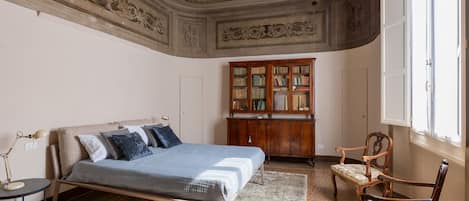 A bedroom with a bed, a wooden cabinet, two chairs, and a window.