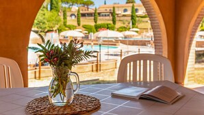 Ein Tisch mit einer klaren Glasvase voller Blumen, einer gewebten Tischmatte und einem offenen Buch, mit Blick auf einen Pool und eine Außenlounge.