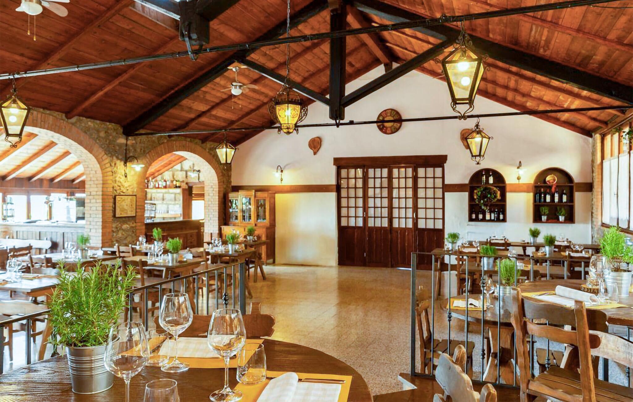 A spacious restaurant with high wooden ceilings, multiple dining tables, and hanging lantern-style lights.