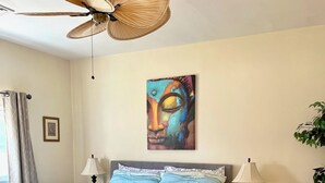A bedroom with a bed, two bedside lamps, a ceiling fan, a painting, and a small table with a lamp.