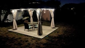 A covered outdoor seating area with a table and chairs, surrounded by a white canopy with string lights.