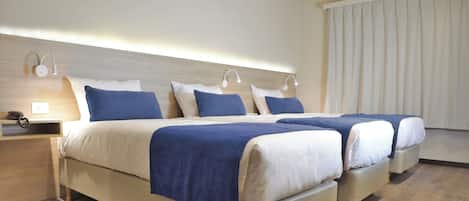 A hotel room with two beds, a bedside table with a phone, and an air conditioning unit above the window.