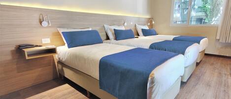 A hotel room with two beds, a wooden floor, a nightstand, and a window with an air conditioning unit.