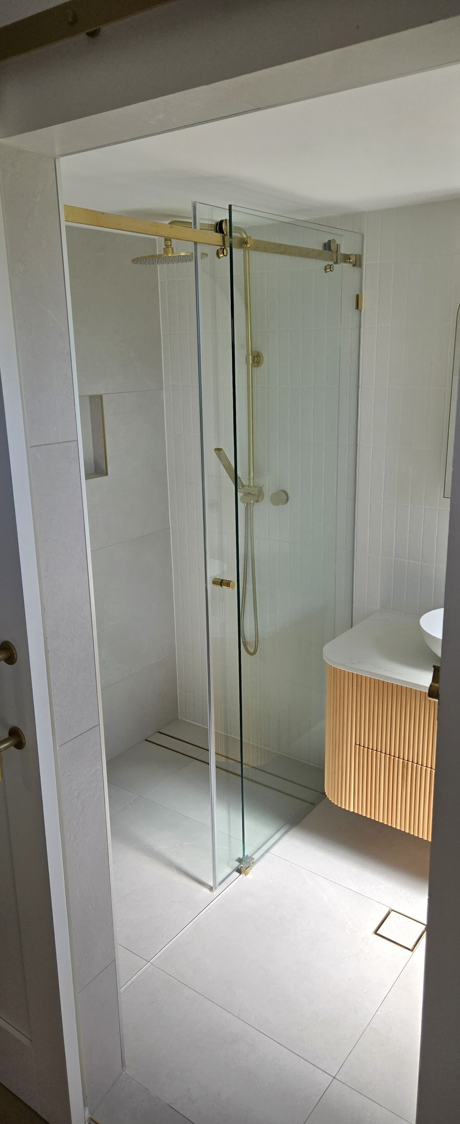 Une salle de bain moderne avec une douche à parois de verre, des murs recouverts de carreaux blancs et un meuble-lavabo en bois.