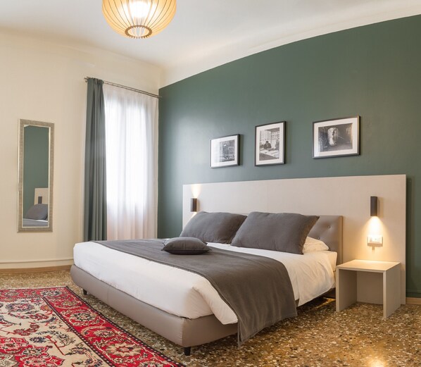 A modern bedroom with a large bed, a red patterned rug, a green wall, and three framed pictures. - Camera 3 - Grand Canal Suites by Wonderful Italy (Venecia)