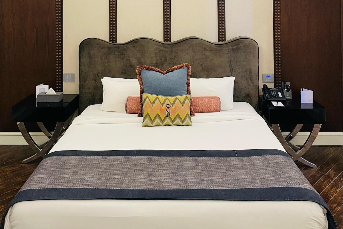 A hotel room with a large bed, two bedside tables, a nightstand, and a headboard with vertical paneling.