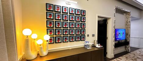 Zona de recepción de un hotel con una pared de obras enmarcadas, un mostrador de recepción con televisor de pantalla plana y una alfombra estampada.