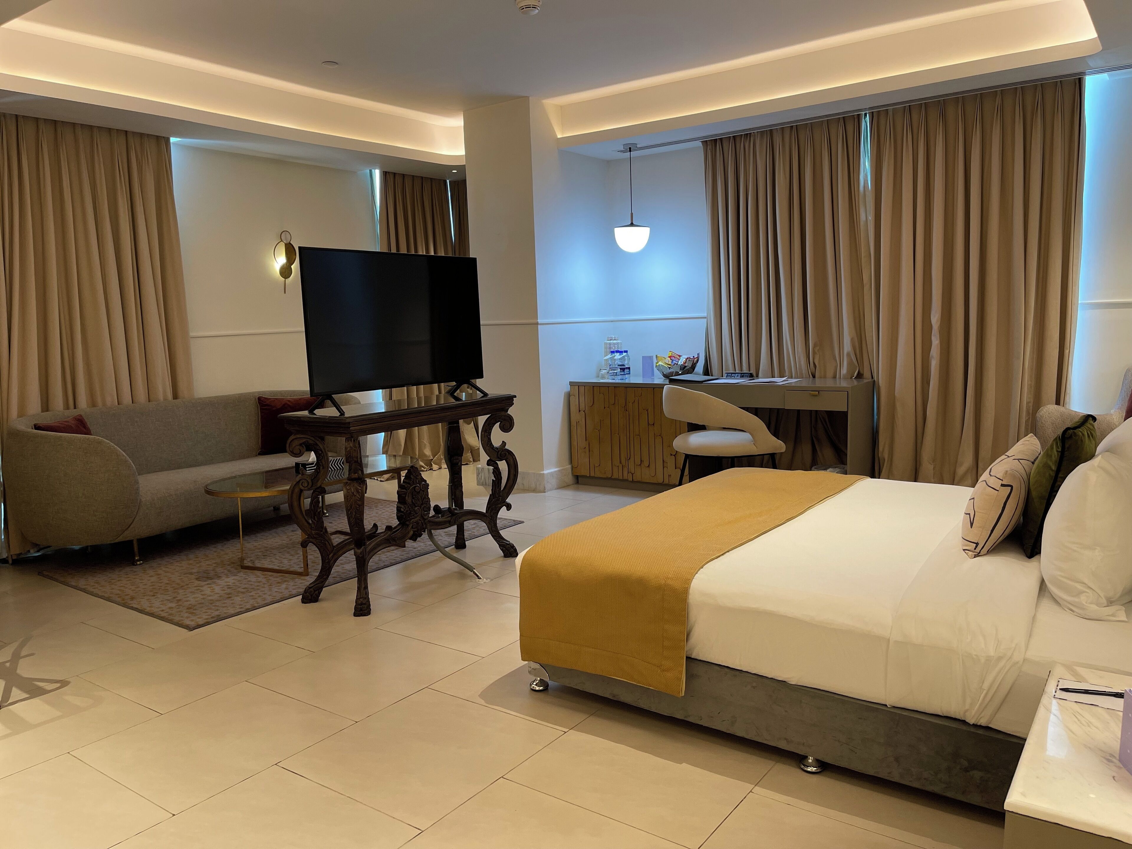 A modern hotel room with a sofa, a bed, a desk, and a TV.
