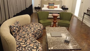 Habitación de hotel con sofá, dos sillones verdes, una mesa de centro de mármol y una cama con cabecera.