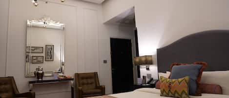 Una habitación de hotel con una cama grande, un escritorio con una silla, un espejo y una araña.
