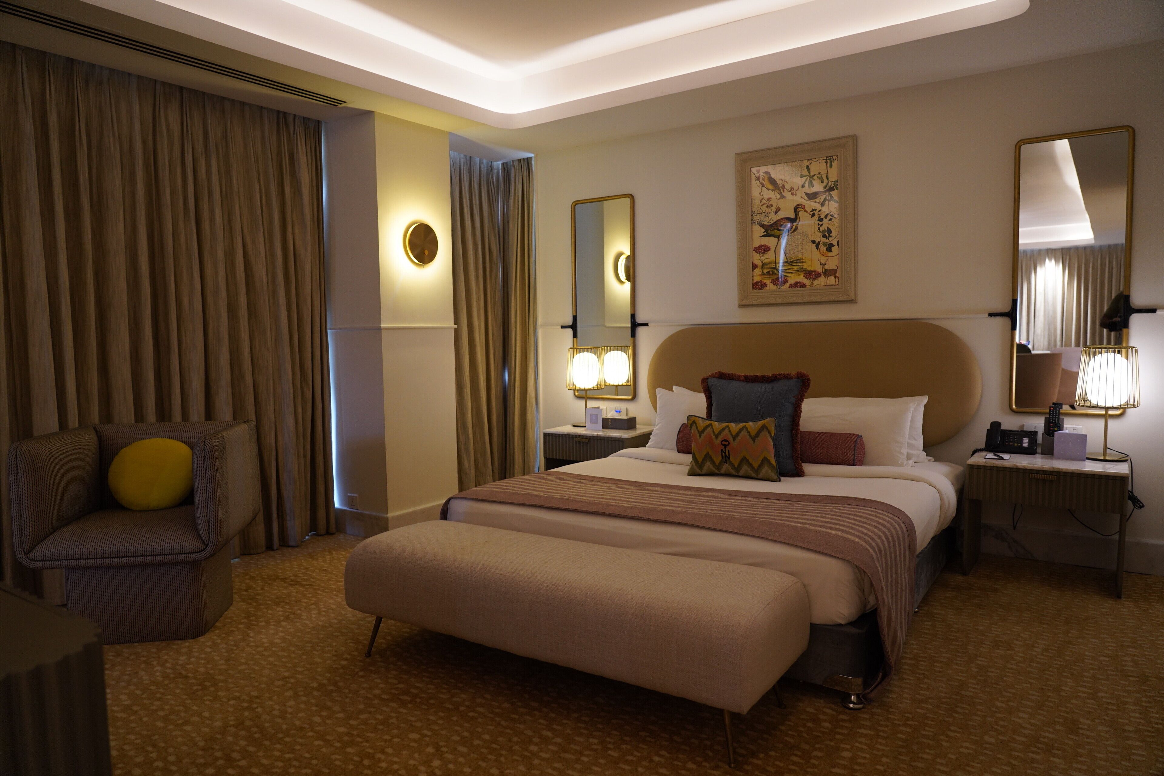 Una habitación de hotel con una cama grande, una silla, una mesita de noche con lámpara y un espejo montado en la pared.