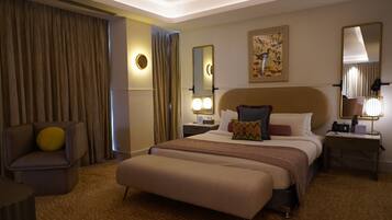 A hotel room with a large bed, a chair, a bedside table with a lamp, and a wall-mounted mirror.