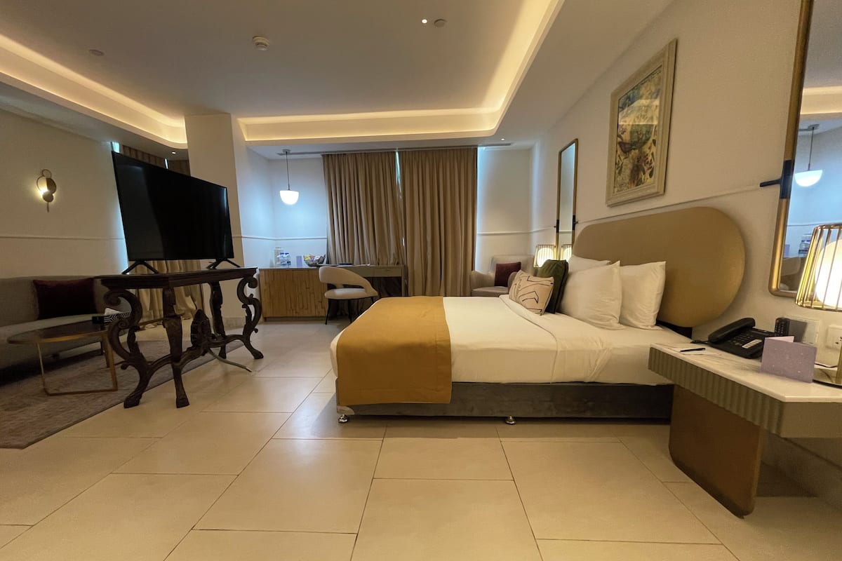 A modern hotel room with a large bed, a desk, a sofa, and a TV.