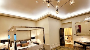 A spacious bedroom with a four-poster bed, a sofa, a desk, and a chandelier. - The Nishat Hotel Gulberg (Lahore)