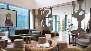 A modern hotel lobby with a sofa set, ottomans, a coffee table, and a decorative wall with cut-out patterns. - The Nishat Hotel Gulberg (Lahore)