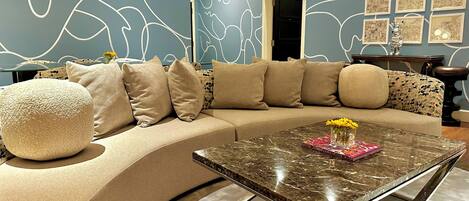 A modern living room with a curved sofa, a glass coffee table, and abstract wall art.