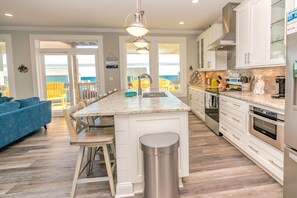 A modern kitchen with white cabinetry, a marble countertop, stainless steel appliances, and a view to the outdoors.