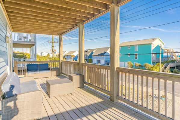 A covered outdoor deck with wicker furniture and a view of neighboring houses.