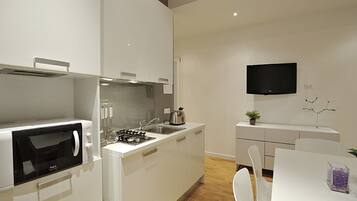 Eine moderne Küche mit weißen Schränken, einer eingebauten Mikrowelle, einem Gasherd und einem Spülbecken. An der Wand ist ein Flachbildfernseher angebracht und auf der Arbeitsfläche steht ein kleiner Blumentopf.