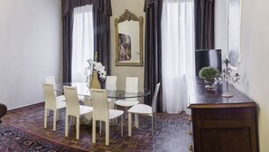 A dining area with a glass table surrounded by chairs, a wooden cabinet, and a chandelier. - San Marco Deluxe Canal View Balcony by Wonderful Italy (Venecia)