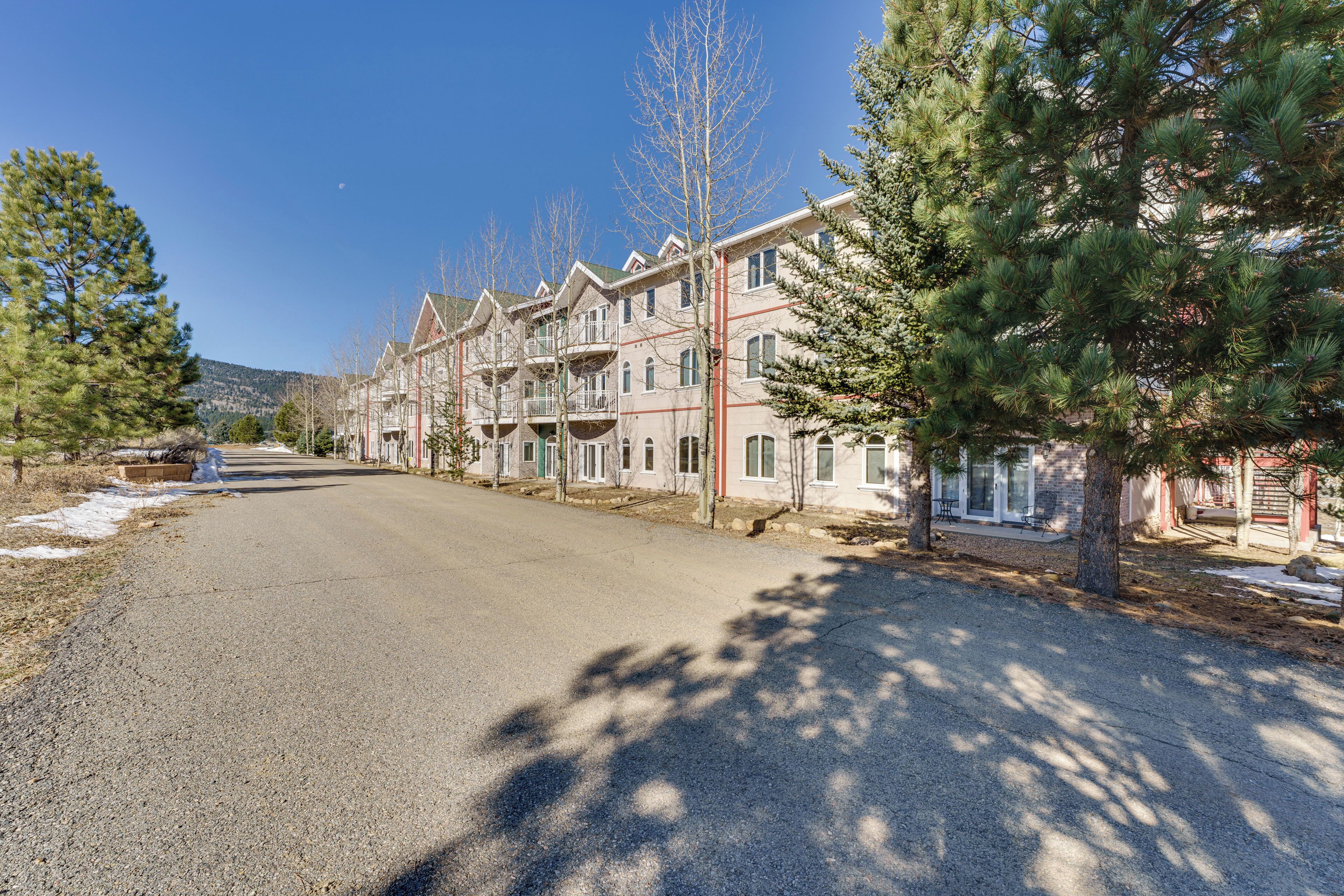 A row of multi-story residential buildings with balconies, a clear sky, and a road in the foreground.