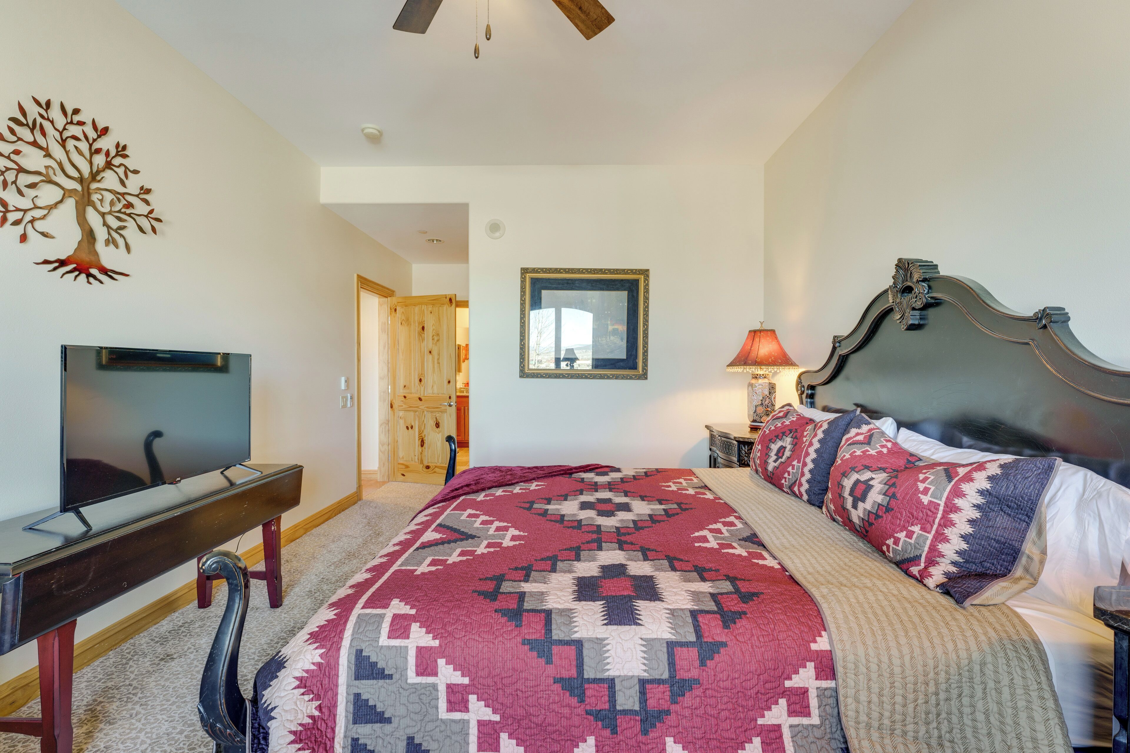 A bedroom with a bed, a TV, a desk, a lamp, and a wall decoration.