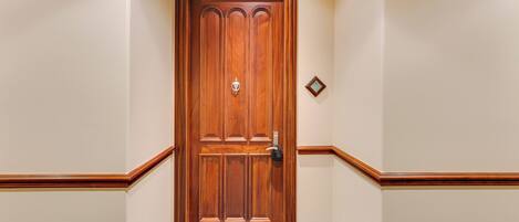 Puerta de madera con manija de latón y cerradura, enmarcada por paredes beige con detalles de madera.