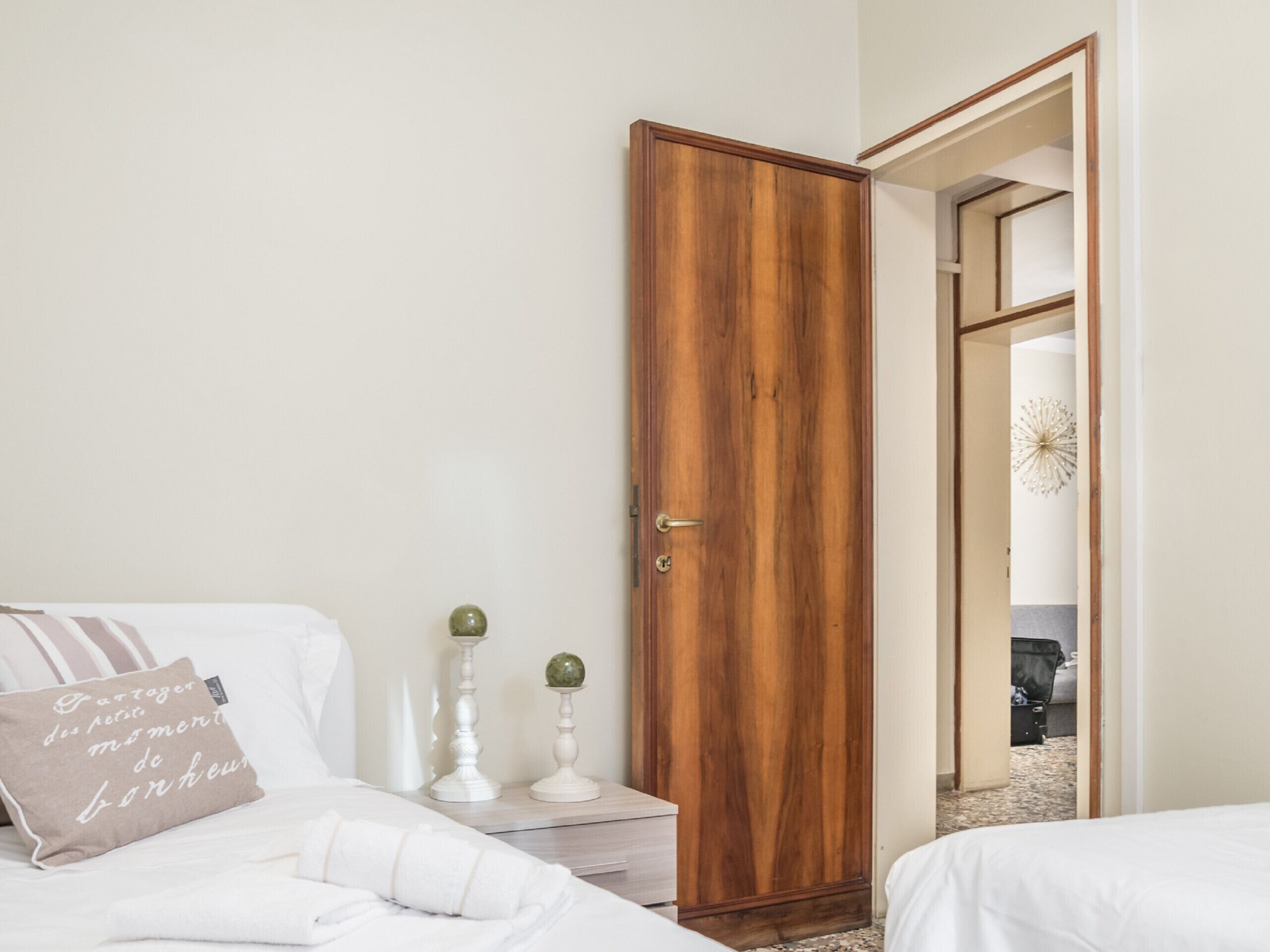 Un dormitorio con un armario de madera, una cama con ropa de cama blanca y una mesita de noche con dos velas.