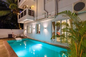 A swimming pool with a white exterior, a balcony with decorative railings, and a view of the surrounding area. - Xenious Micro Villas Goa (Vagator)