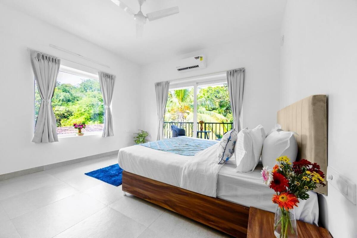 A bedroom with a bed, a window with curtains, a ceiling fan, and a view of greenery outside.