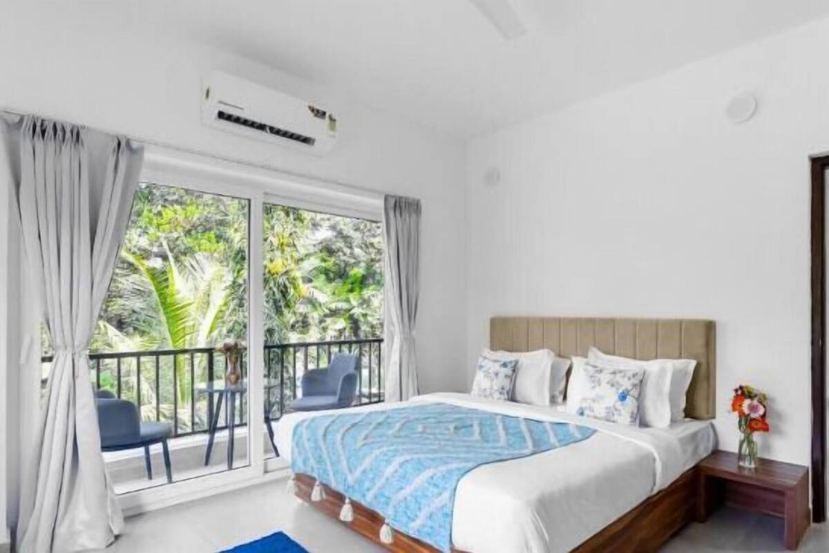 A bedroom with a large bed, a balcony with a chair, and a view of greenery outside.