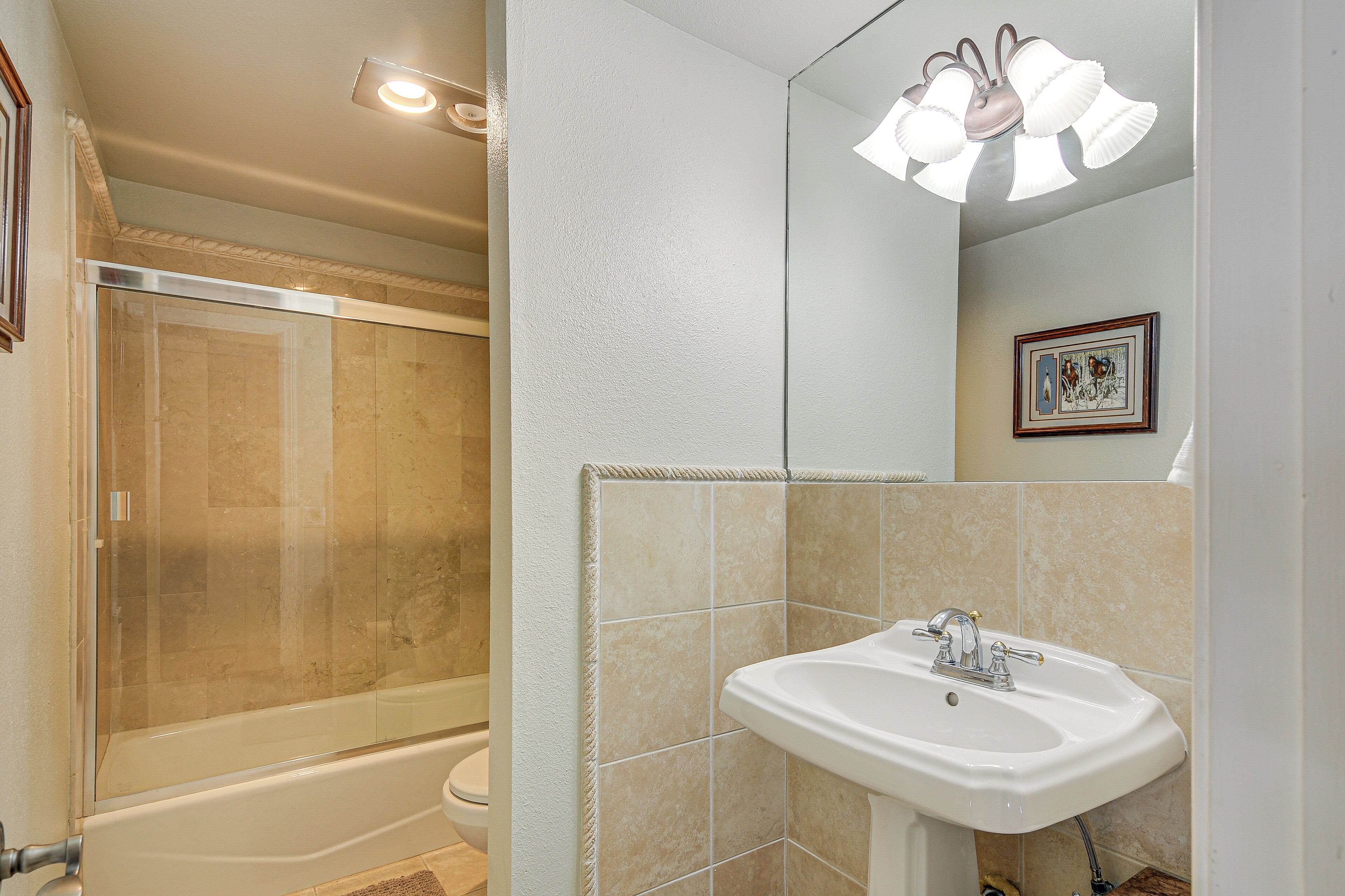 A bathroom with a glass-enclosed shower, a white sink, and a mirror with a light fixture.