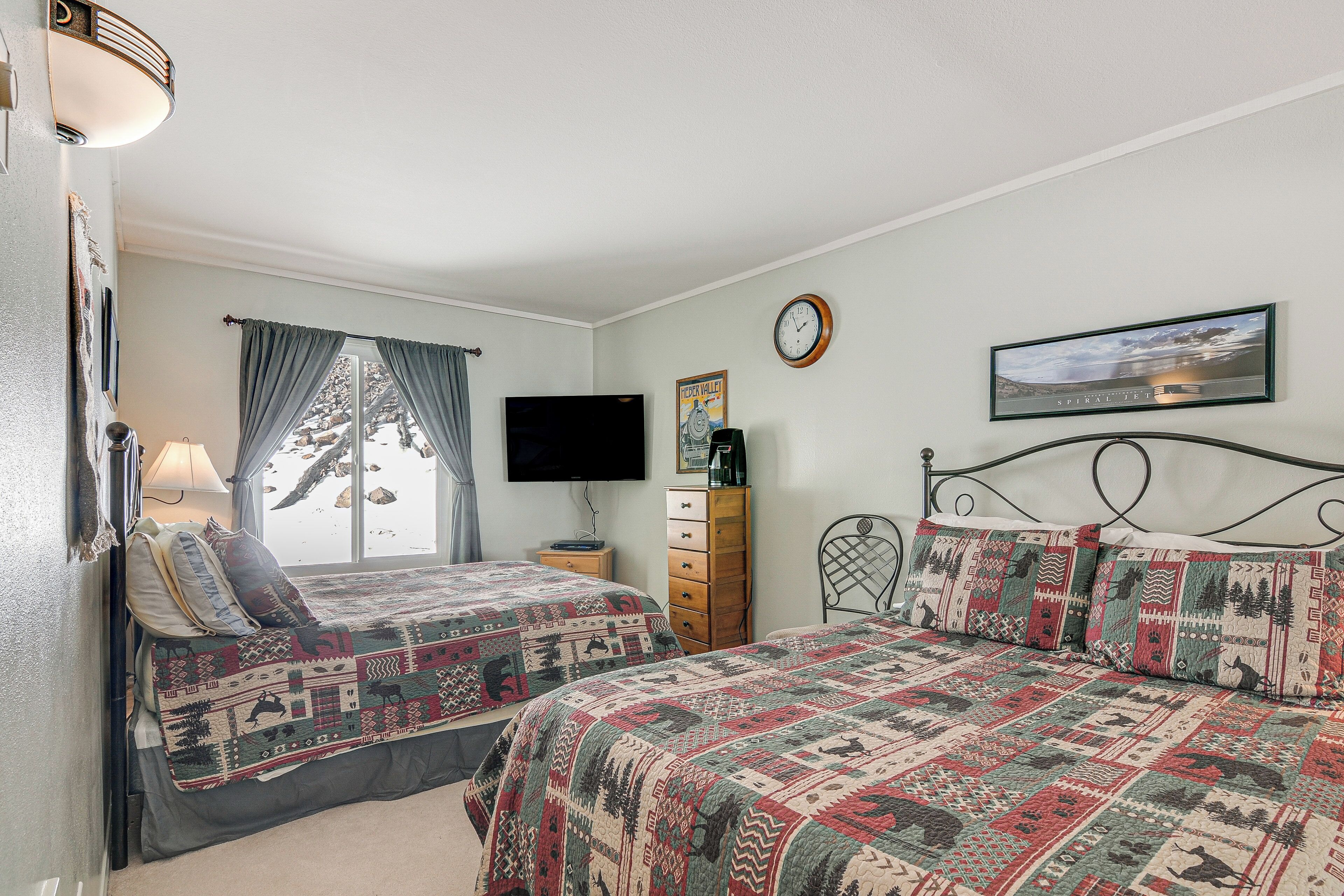 A bedroom with two beds, a dresser, a television, and a clock on the wall.