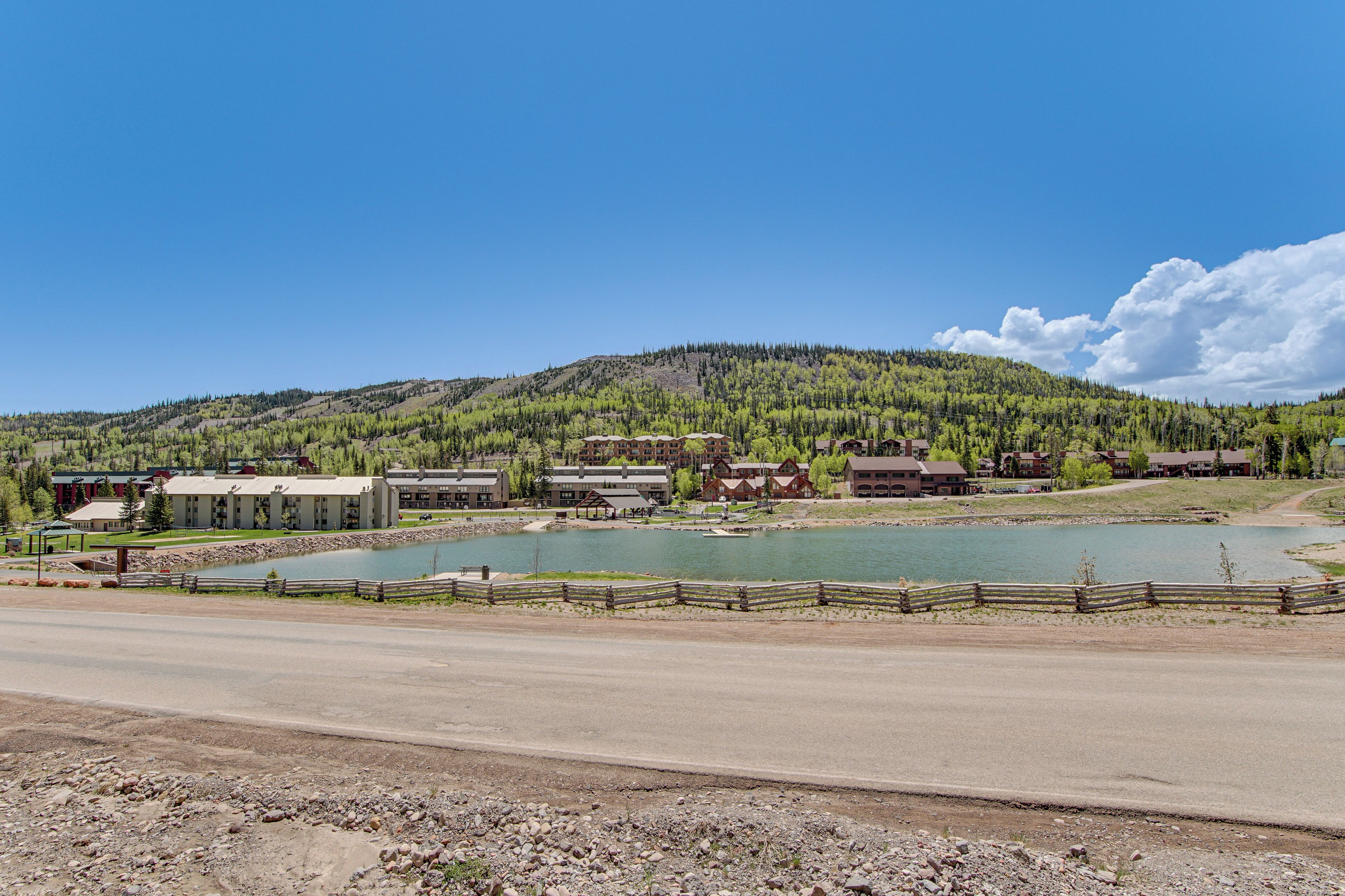 A lakeside resort with multiple buildings, a wooden dock, and a clear view of the lake and surrounding mountains.