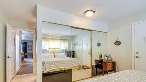 A bedroom with a large mirror, a bed with patterned bedding, a bedside table with a fan, and a door leading to another room. - Hike, Bike & Fish: Brian Head Resort Condo! (Brian Head)