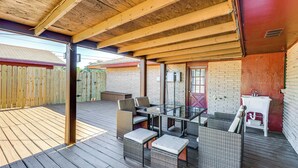 Une terrasse extérieure couverte, dotée d’une table en verre et de meubles en osier.