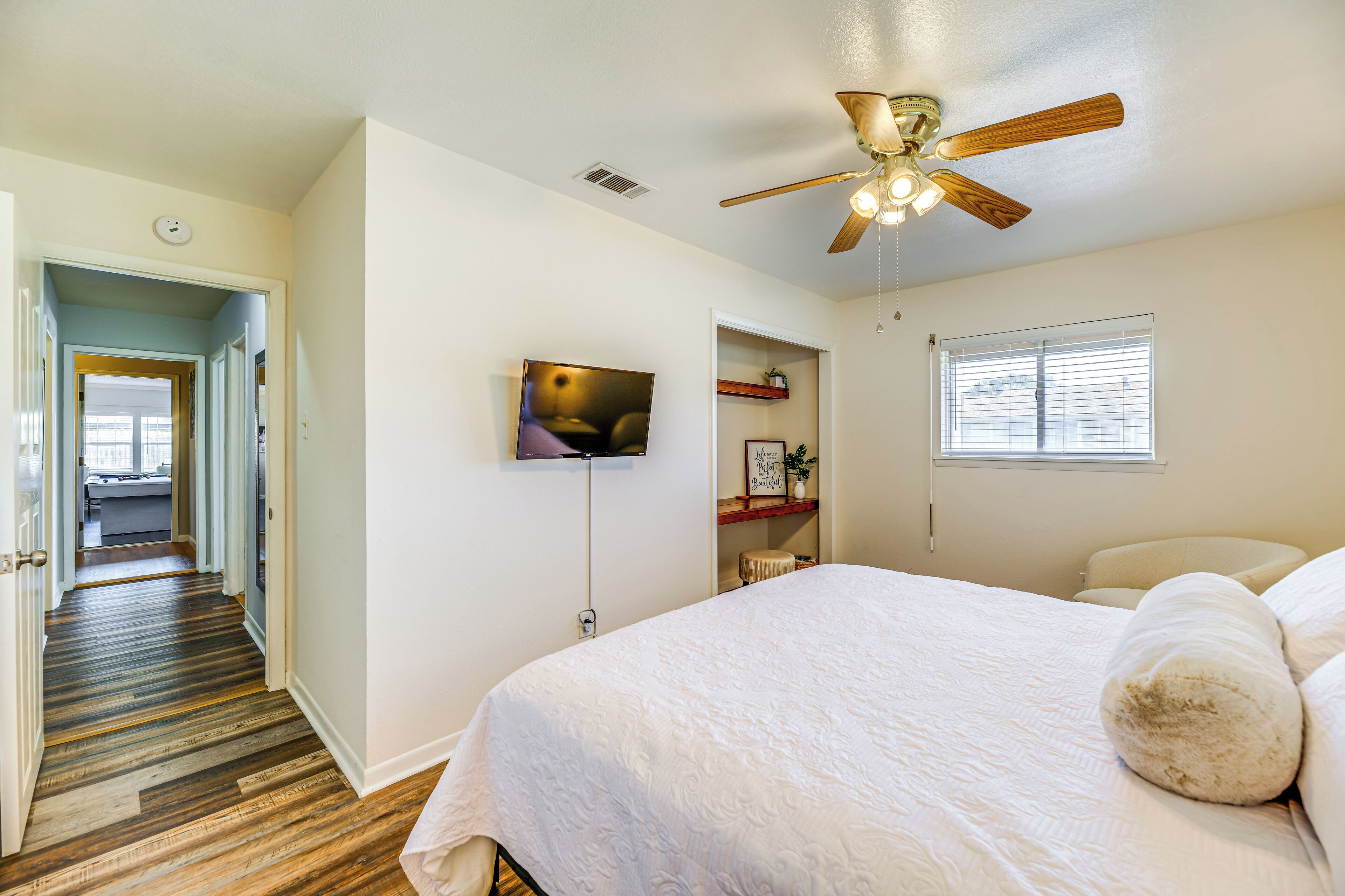 A bedroom with a large bed, a ceiling fan, a TV, and a window with blinds.