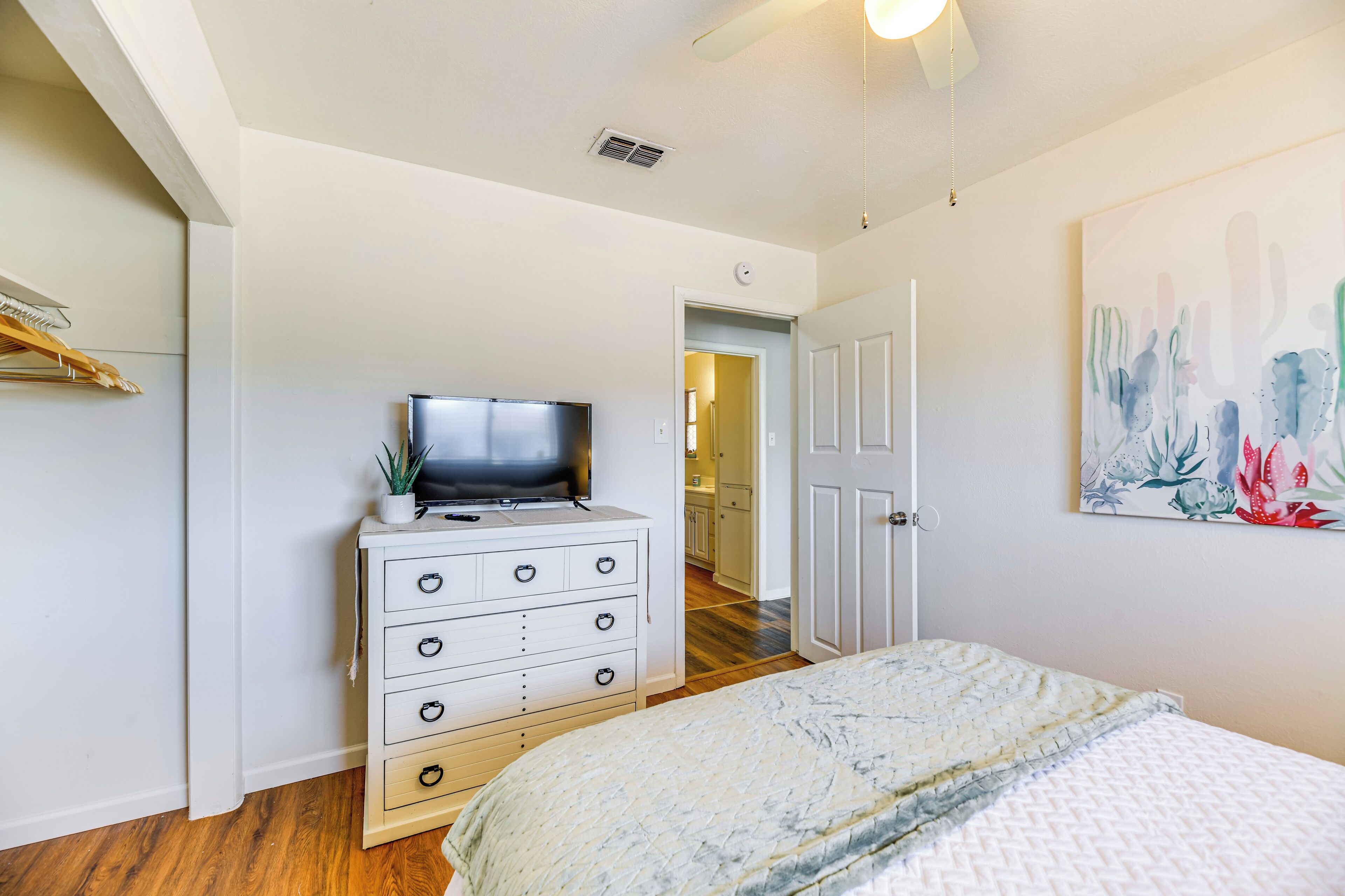 Un dormitorio con cama, cómoda con televisor, puerta y un cuadro en la pared.