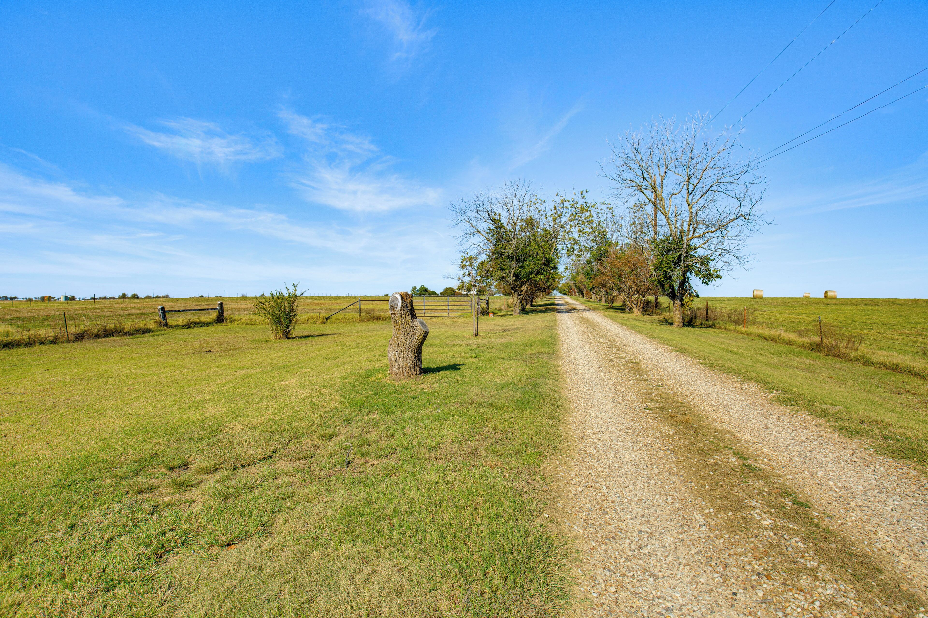Une route de campagne menant à un portail, avec un arbre et des bottes de foin en arrière-plan.
