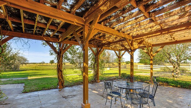 Een overdekt terras met een tafel en stoelen, omgeven door een houten pergola.