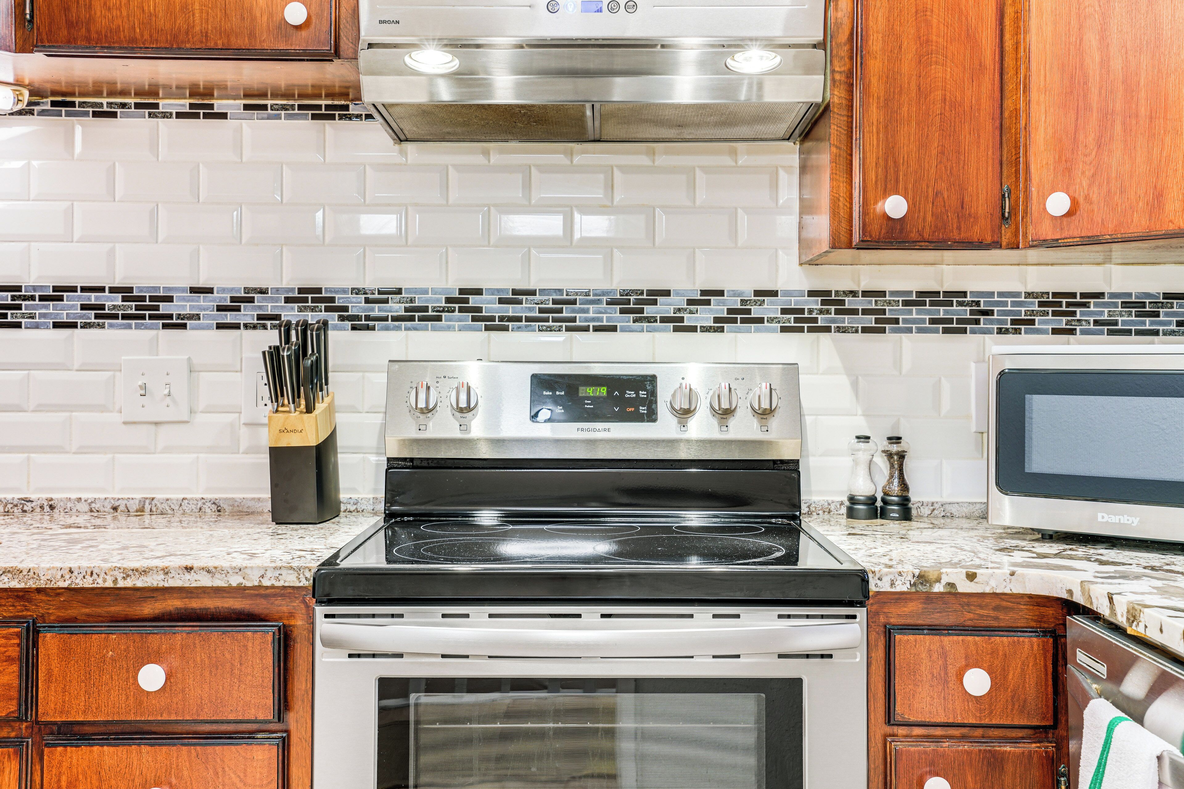 A kitchen with a stainless steel stove, white tiled backsplash, wooden cabinets, and a microwave.
