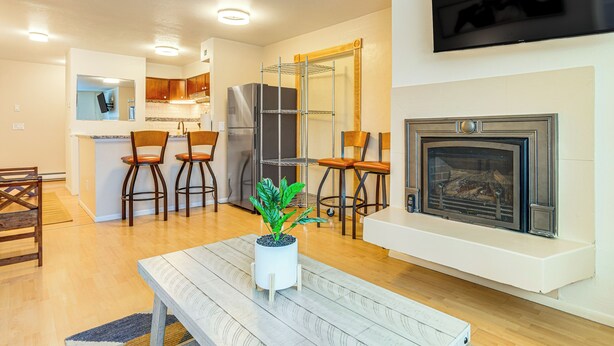 A modern kitchen with wooden cabinets, a stainless steel refrigerator, and a built-in oven. There is a dining area with a wooden table and chairs, and a living room with a fireplace. - 1 Mi to Dtwn: Cozy Condo in Anchorage! (Anchorage)
