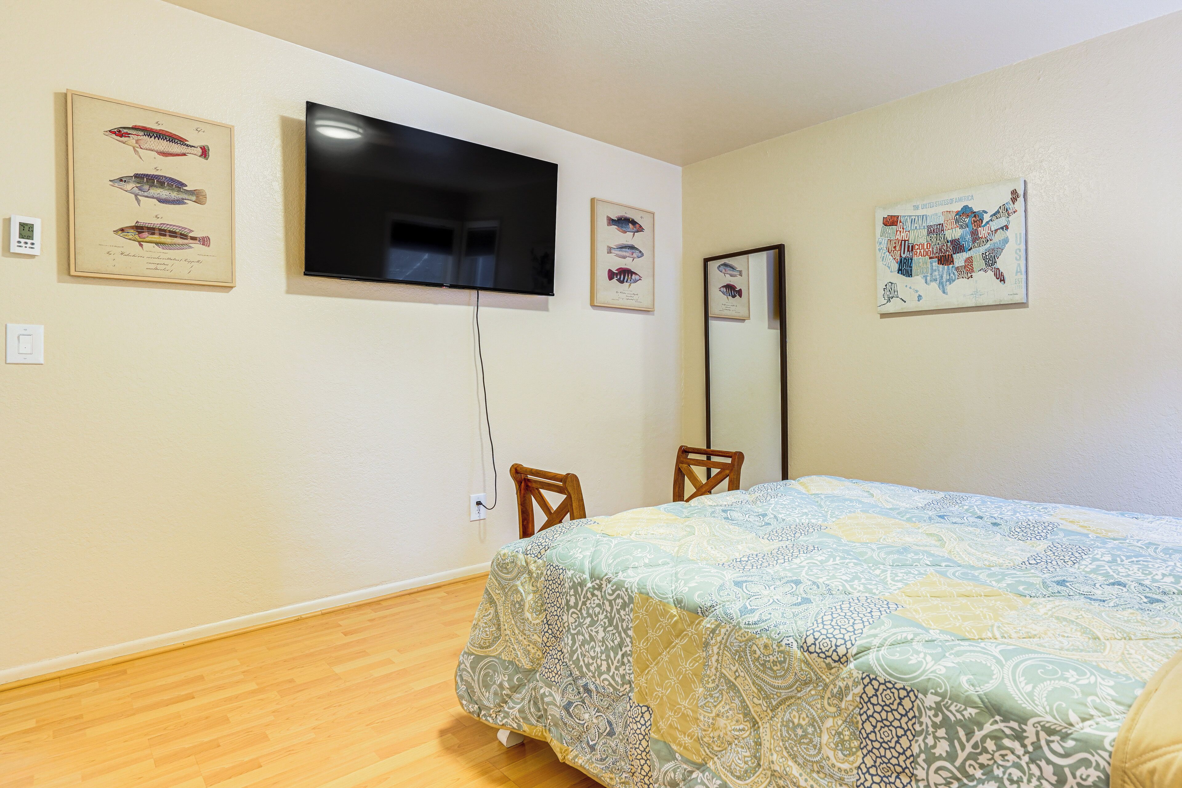 A bedroom with a bed, a television mounted on the wall, and framed fish illustrations.
