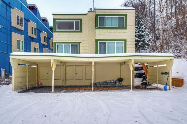 A covered outdoor area with a barbecue grill, a snow-covered ground, and a building with multiple windows and a green trim. - 1 Mi to Dtwn: Cozy Condo in Anchorage! (Anchorage)